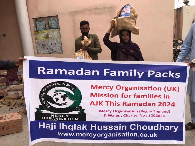 A Ramadan Family Packs banner held up while families carry food sacks behind it.