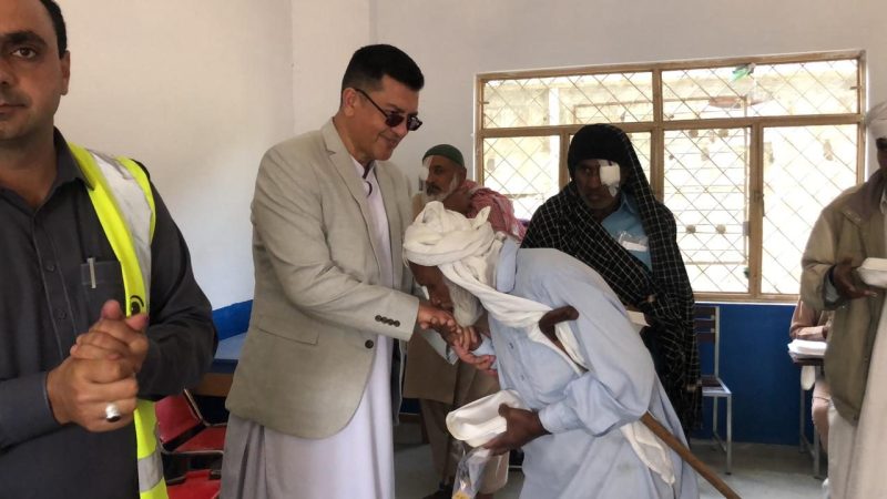 Team members helping an elderly woman with a walking stick at a free eye camp.