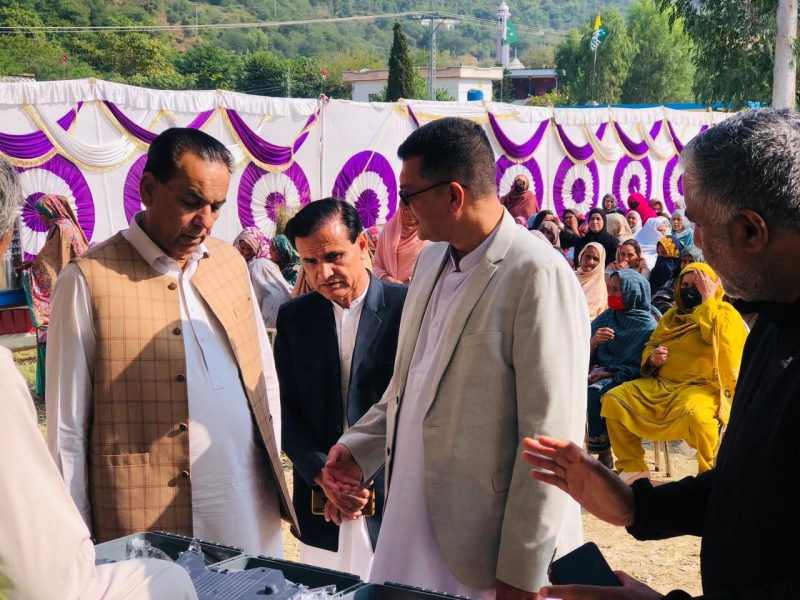 Men greeting each other at an outdoor community event under a decorated canopy.