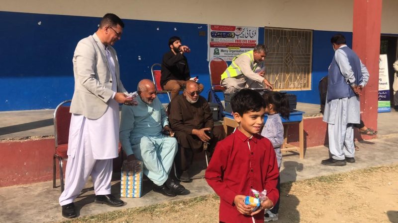 Elderly men and a young boy waiting in a school courtyard during a free eye camp.