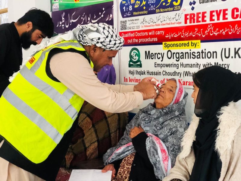 A volunteer in a high-visibility vest putting eye drops into an elderly woman's eye.