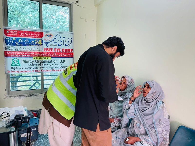 A doctor and a volunteer checking the eyes of two women at a free eye camp.